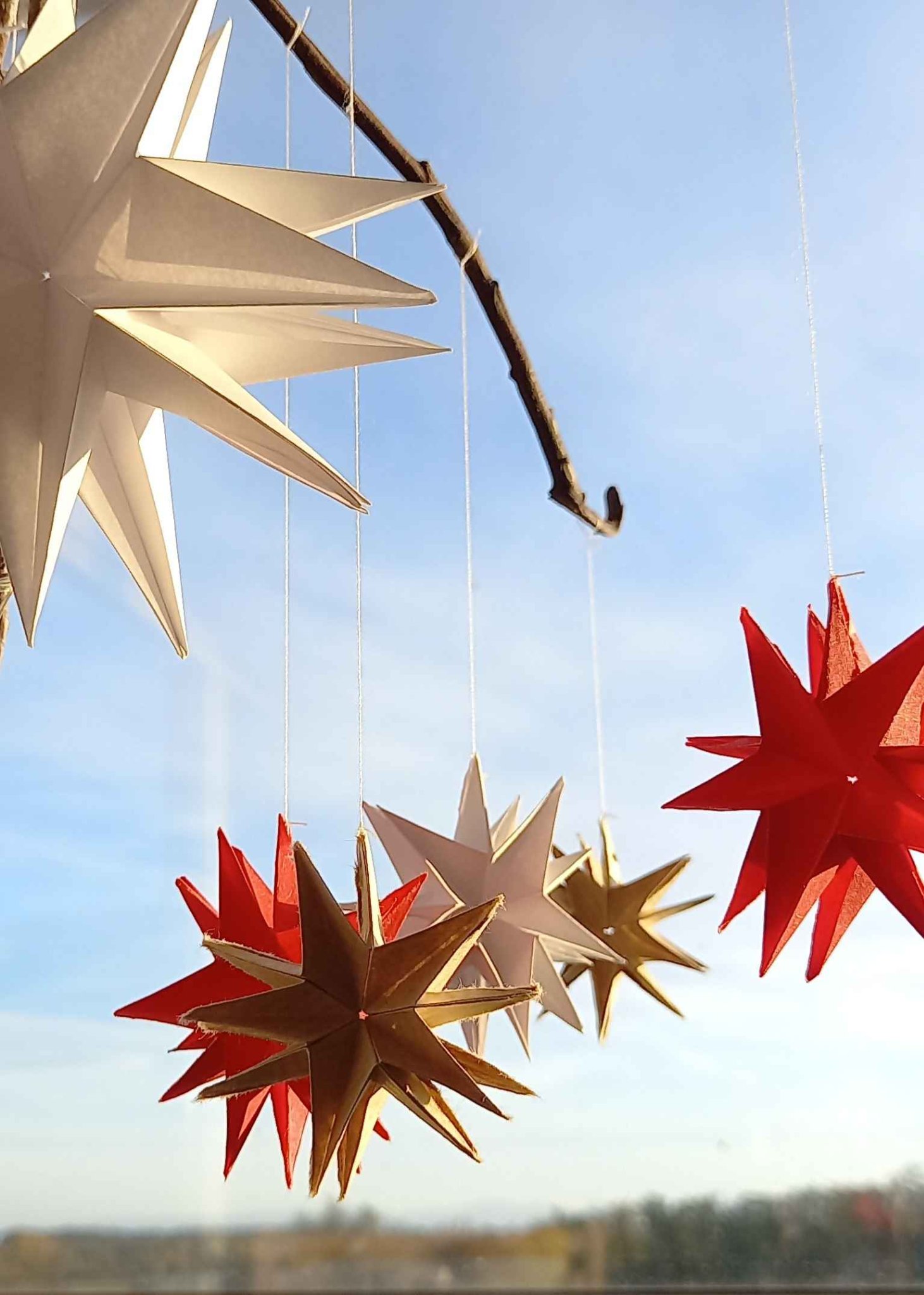 Quelques étoiles (rouges, blanches, "dorées") en origami suspendues par des fils à des brindilles trouvées au jardin. Elles sont prises en photo dans la lumière du soleil couchant. Quelques étoiles (rouges, blanches, "dorées") en origami suspendues par des fils à des brindilles trouvées au jardin. Elles sont prises en photo dans la lumière du soleil couchant.