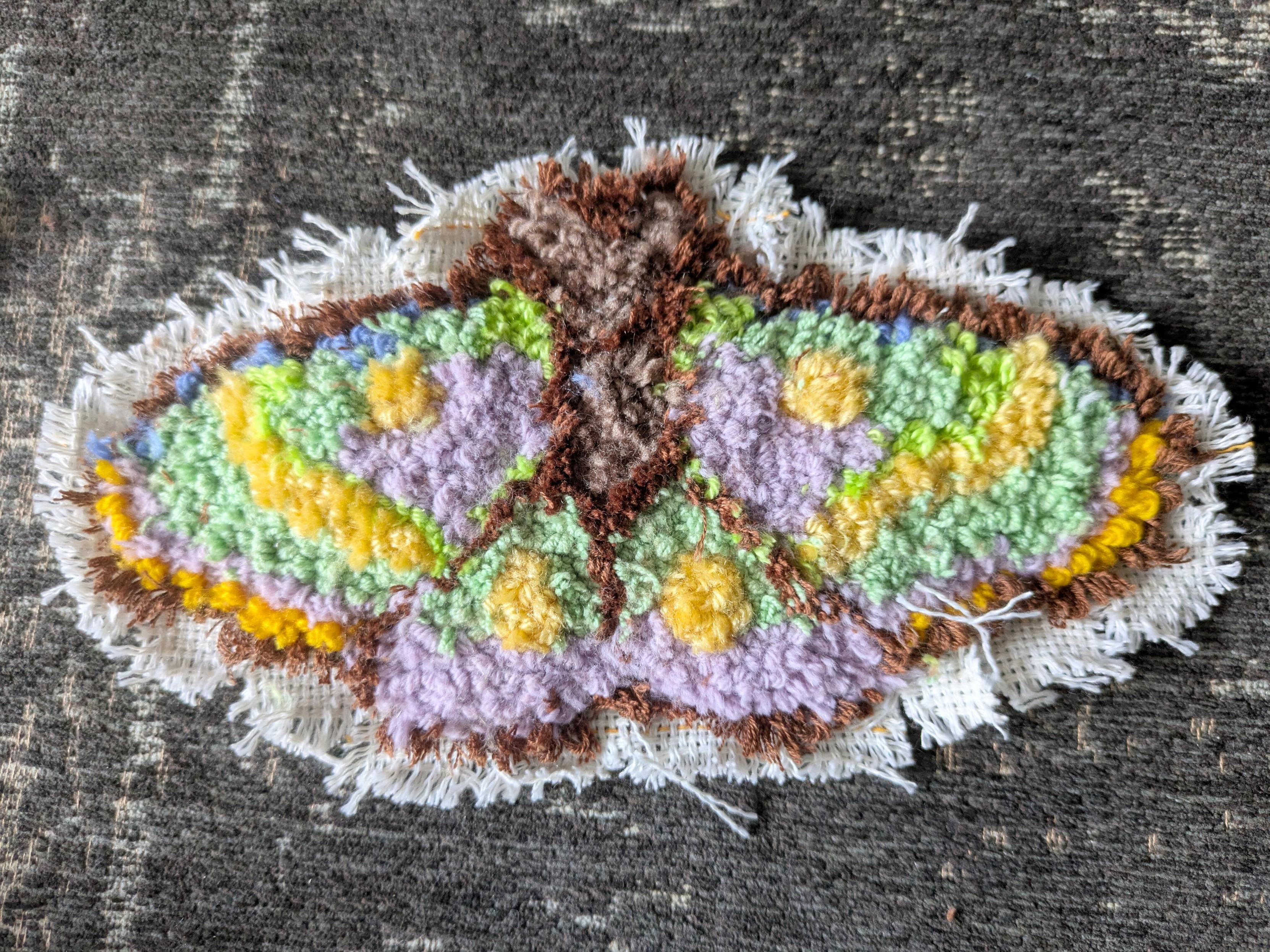 Punch needle d'un papillon de nuit au contour marron. Les ailes sont violettes, vertes et jaunes Punch needle d'un papillon de nuit au contour marron. Les ailes sont violettes, vertes et jaunes