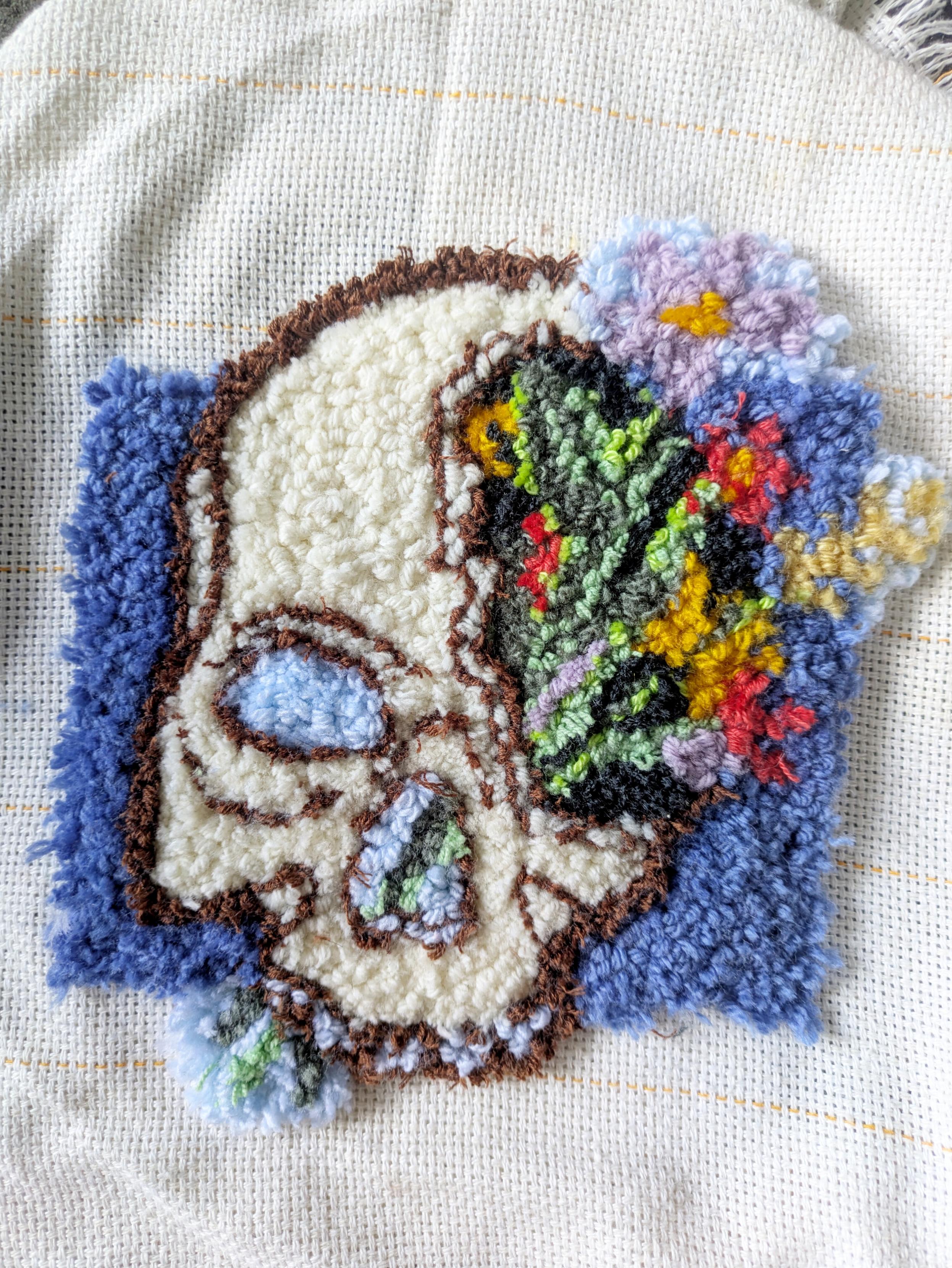 Punch needle d'un crâne sur fond bleu. La moitié est fendue et il en sort un bouquet de fleur Punch needle d'un crâne sur fond bleu. La moitié est fendue et il en sort un bouquet de fleur