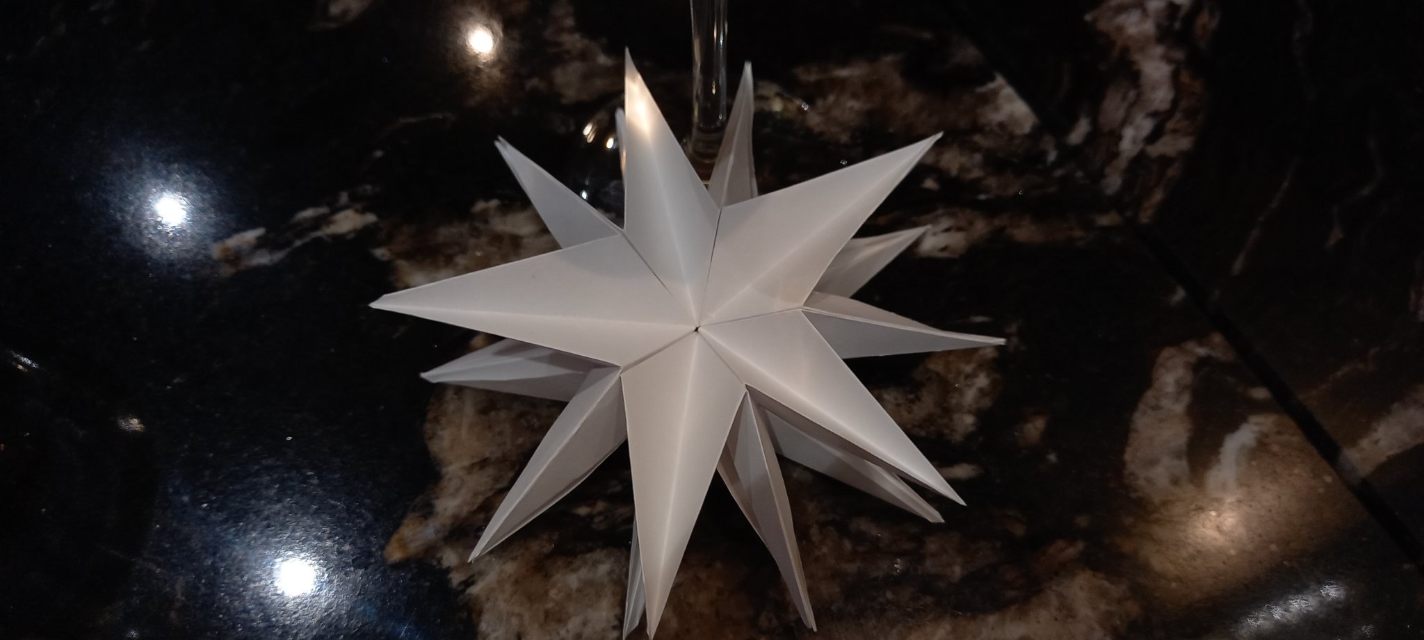 Une étoile à 5 branches principales en papier blanc en origami posée sur la table en marbre d'un bistrot Une étoile à 5 branches principales en papier blanc en origami posée sur la table en marbre d'un bistrot