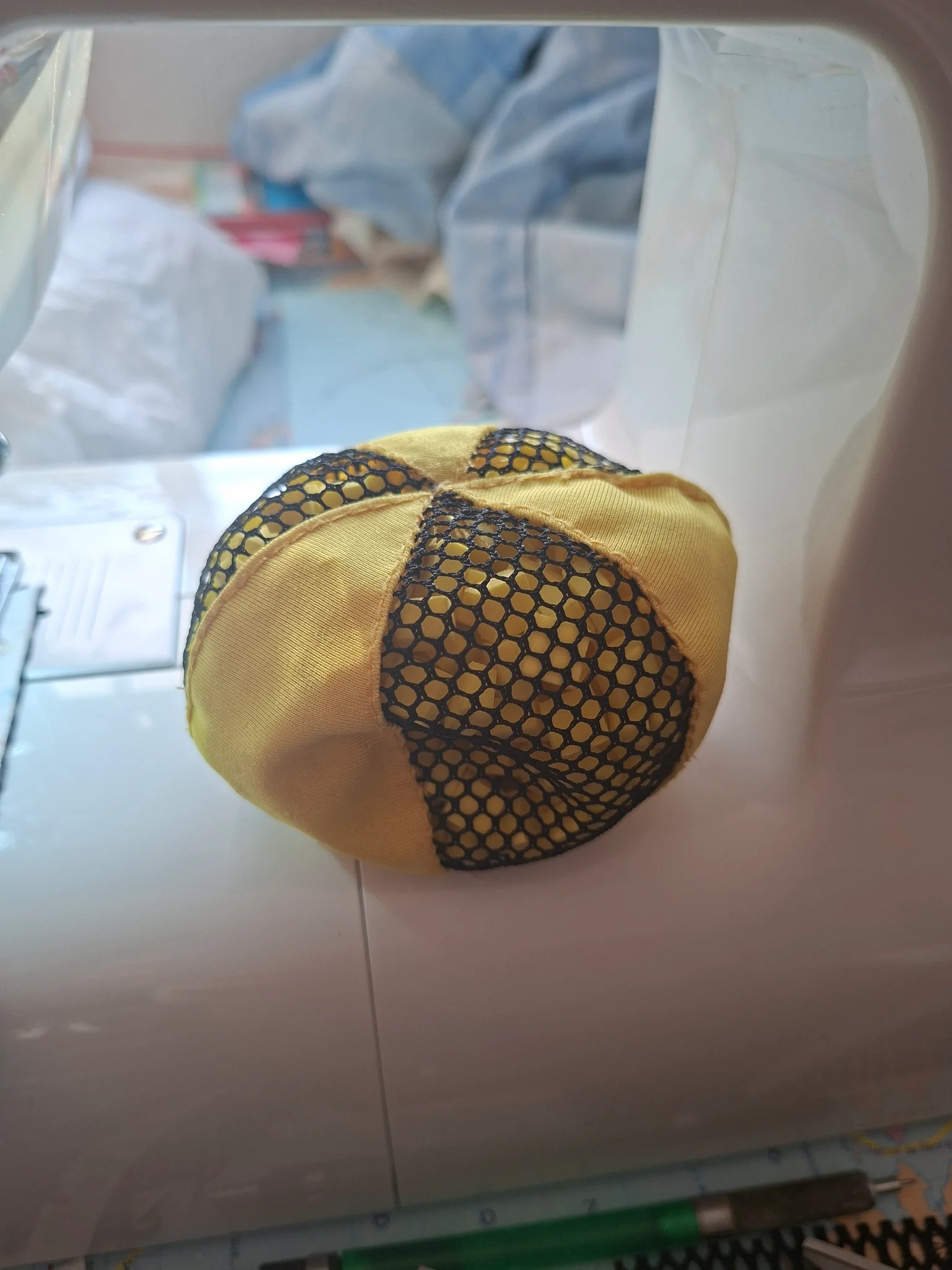 une balle en tissu, composée de 6 sections alternées de coton fin jaune moutarde, et de sections de mesh noir. Elle semble rembourrée avec des petits éléments. Les coutures sont nettes et bien plates, la jointure aux poles est précise. Elle est posée sur une surface carrelée une balle en tissu, composée de 6 sections alternées de coton fin jaune moutarde, et de sections de mesh noir. Elle semble rembourrée avec des petits éléments. Les coutures sont nettes et bien plates, la jointure aux poles est précise. Elle est posée sur une surface carrelée