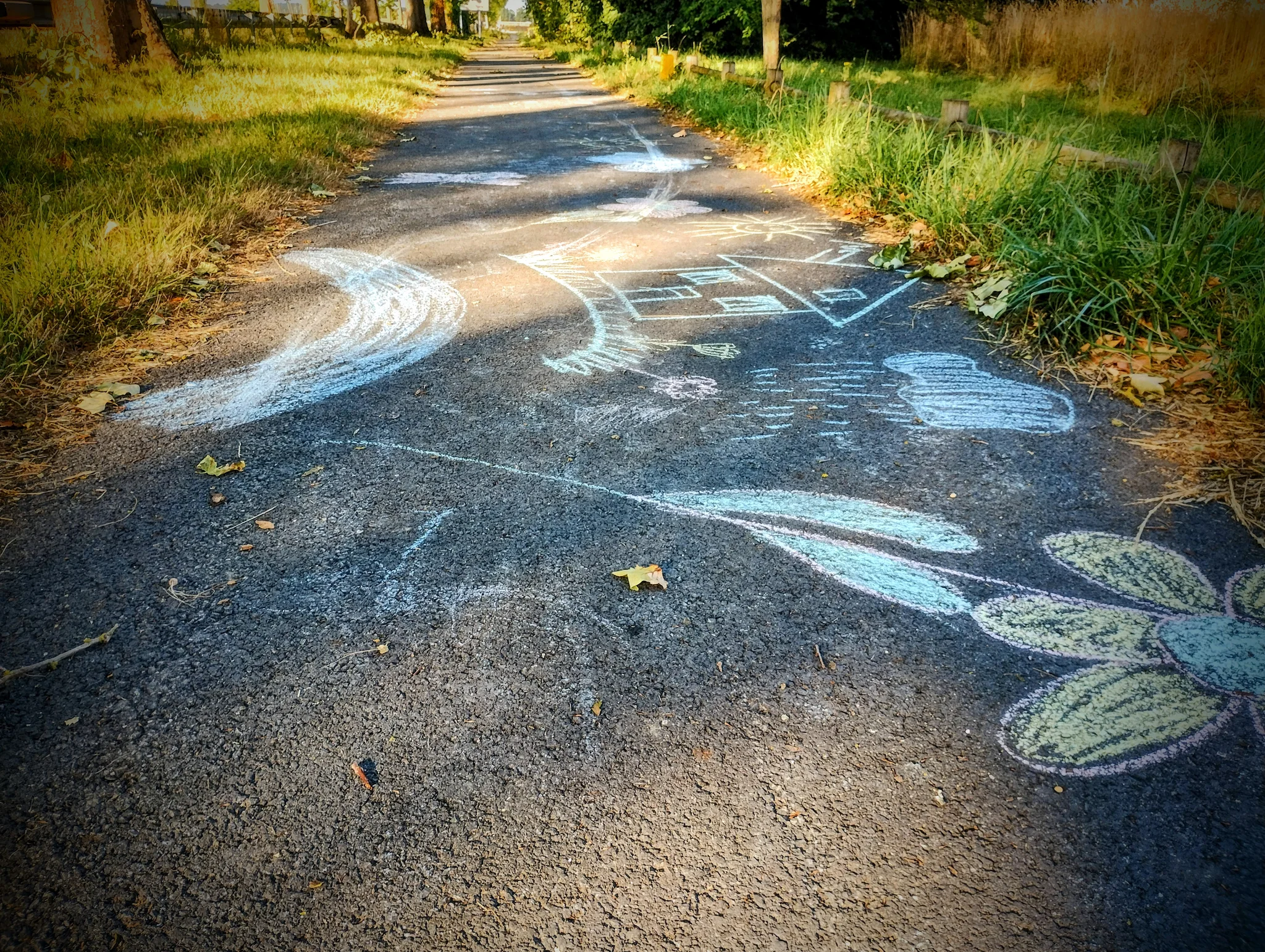 Dessin d'enfants à la craie sur un chemin en bitume, jalonné d'herbe et arbres Dessin d'enfants à la craie sur un chemin en bitume, jalonné d'herbe et arbres